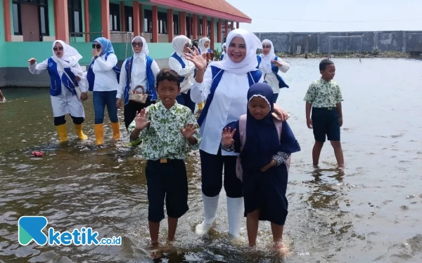 Foto Sekretaris DPC IWAPI Sidoarjo Yuniar Safitri bersama pengurus lain, serta murid-murid melewati genangan air di halaman SDN Banjarasri, Tanggulangin. (Foto: Fathur Roziq/Ketik.co.id)